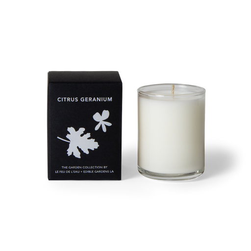 Explore our 3oz citrus geranium candle, blending lemon bergamot, lavender, and geranium. Hand-poured with apricot and coconut wax in LA, and part of the Garden Collection, a Le Feu De L’eau and Lauri Kranz collaboration. Cruelty-free, natural fragrance, no harmful additives, phthalates, parabens, sulfates, and more. The candle sits outside its black box, against a white surface. The second hover image shows the candle sitting against a background of an up close pink grapefruit.