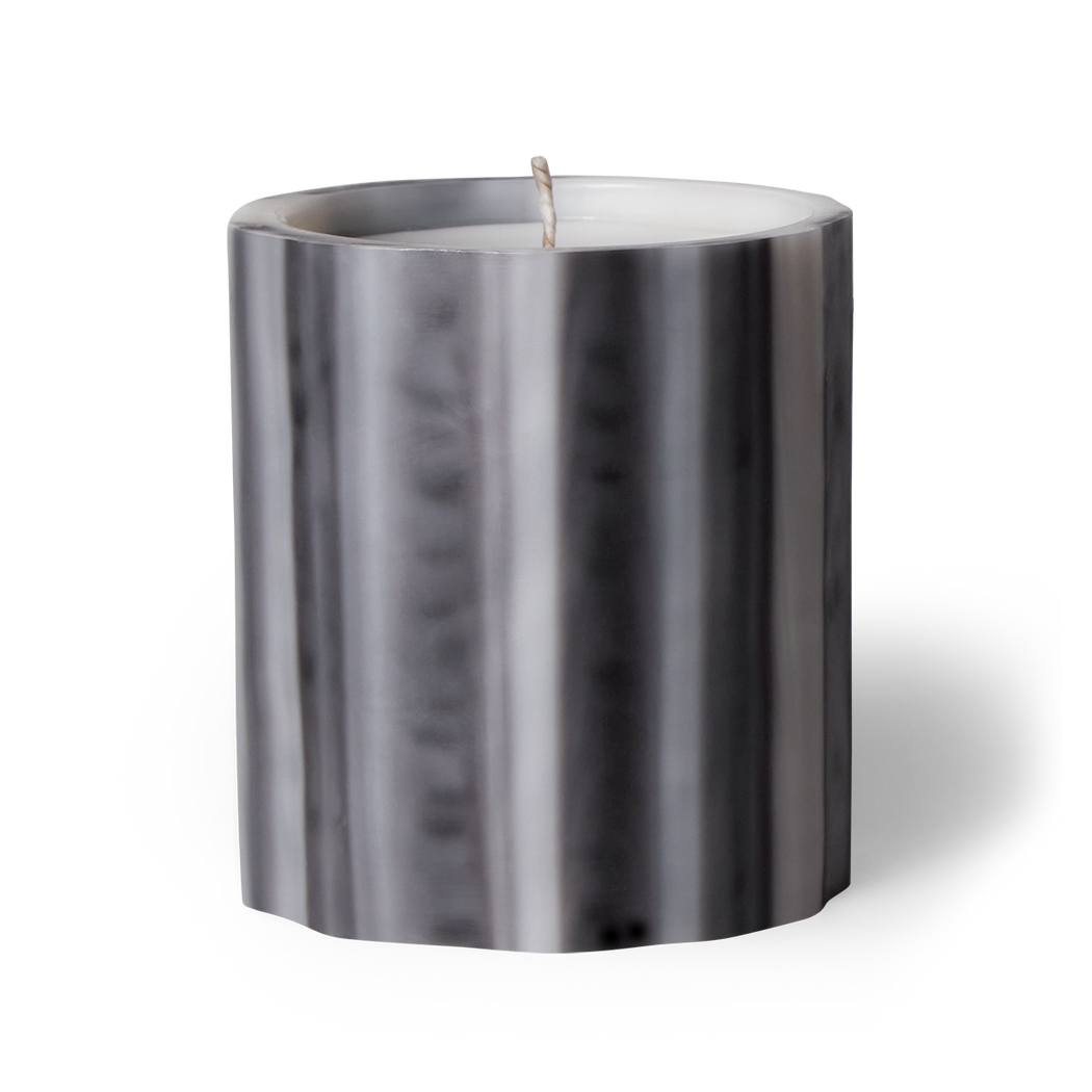 Elevate your ambiance with gris scented artisanal candle by Le Feu De L'eau. Experience the allure of clove, musk, and sandalwood, perfect for the magic hour. Handcrafted underwater from wax, each candle is unique. Hand-poured in LA with coconut apricot wax. Enjoy 75 hours of burn time. Natural fragrance. Non-toxic. Image of gris scented candle in grey colored wax vessel.