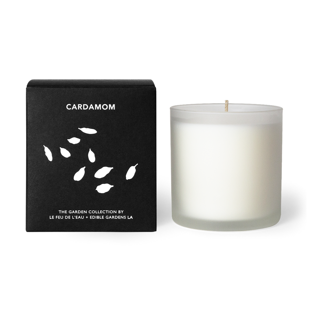 A 12oz candle blending cardamom, parsley, and coriander. Hand-poured with apricot and coconut wax in Los Angeles, part of the Garden Collection, a collaboration between Le Feu De L’eau and Lauri Kranz of Edible Gardens LA. The candle sits beside the black box, against a white surface. The second hover image shows the candle against an up close image of green cardamom pods.