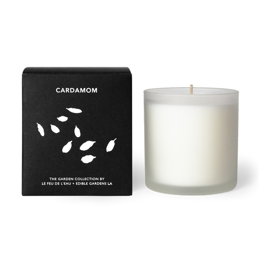 A 12oz candle blending cardamom, parsley, and coriander. Hand-poured with apricot and coconut wax in Los Angeles, part of the Garden Collection, a collaboration between Le Feu De L’eau and Lauri Kranz of Edible Gardens LA. The candle sits beside the black box, against a white surface. The second hover image shows the candle against an up close image of green cardamom pods.