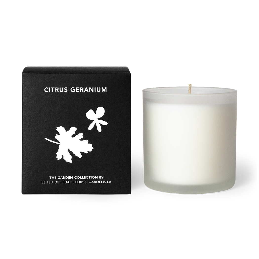 A 12oz candle blending lemon bergamot, lavender and geranium. Hand-poured with apricot and coconut wax in Los Angeles, part of the Garden Collection, a collaboration between Le Feu De L’eau and Lauri Kranz of Edible Gardens LA.  It sits beside the black box, against a white surface. The second hover image shows the candle sitting against a background of an up close pink grapefruit. 