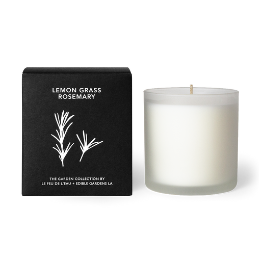 Discover our 12oz lemon grass rosemary candle, part of an inspiring collaboration between Le Feu De L’Eau and garden designer Lauri Kranz of Edible Gardens LA. Hand-poured with apricot and coconut wax. Made in Los Angeles. The candle sits outside of its black box, against a white surface. The second hover image shows the candle sitting against an up close background of green rosemary plants.
