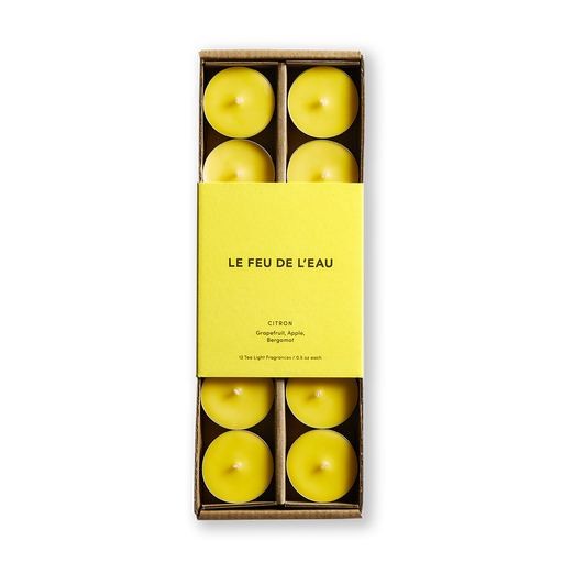 Awaken your senses with Citron Tea Lights. Invigorating notes of Grapefruit, Apple, and Bergamot greet each new day. Hand-poured in LA, these cruelty-free delights feature coconut apricot wax and lead-free cotton wicks. Elevate your ambiance with this set of 12 | .5oz Tea Lights. Image is of the yellow tea light candles in a box with matching yellow colored packaging.