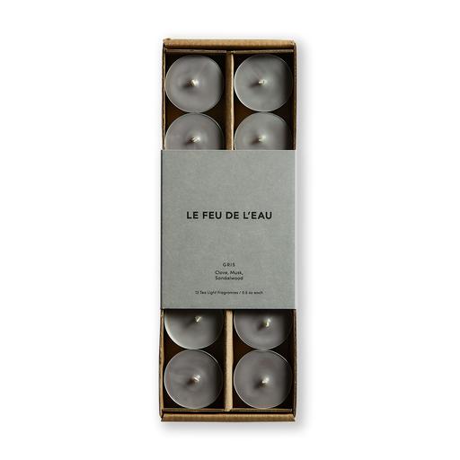 Experience the allure of Gris tea lights infused with clove, musk, and sandalwood. Each set contains 12 tea lights, meticulously poured in small batches in Los Angeles. Enjoy cruelty-free, coconut apricot wax with natural fragrance, lead-free cotton wicks, and no harmful additives. The image is of the grey tea lights in box with matching grey packaging. 
