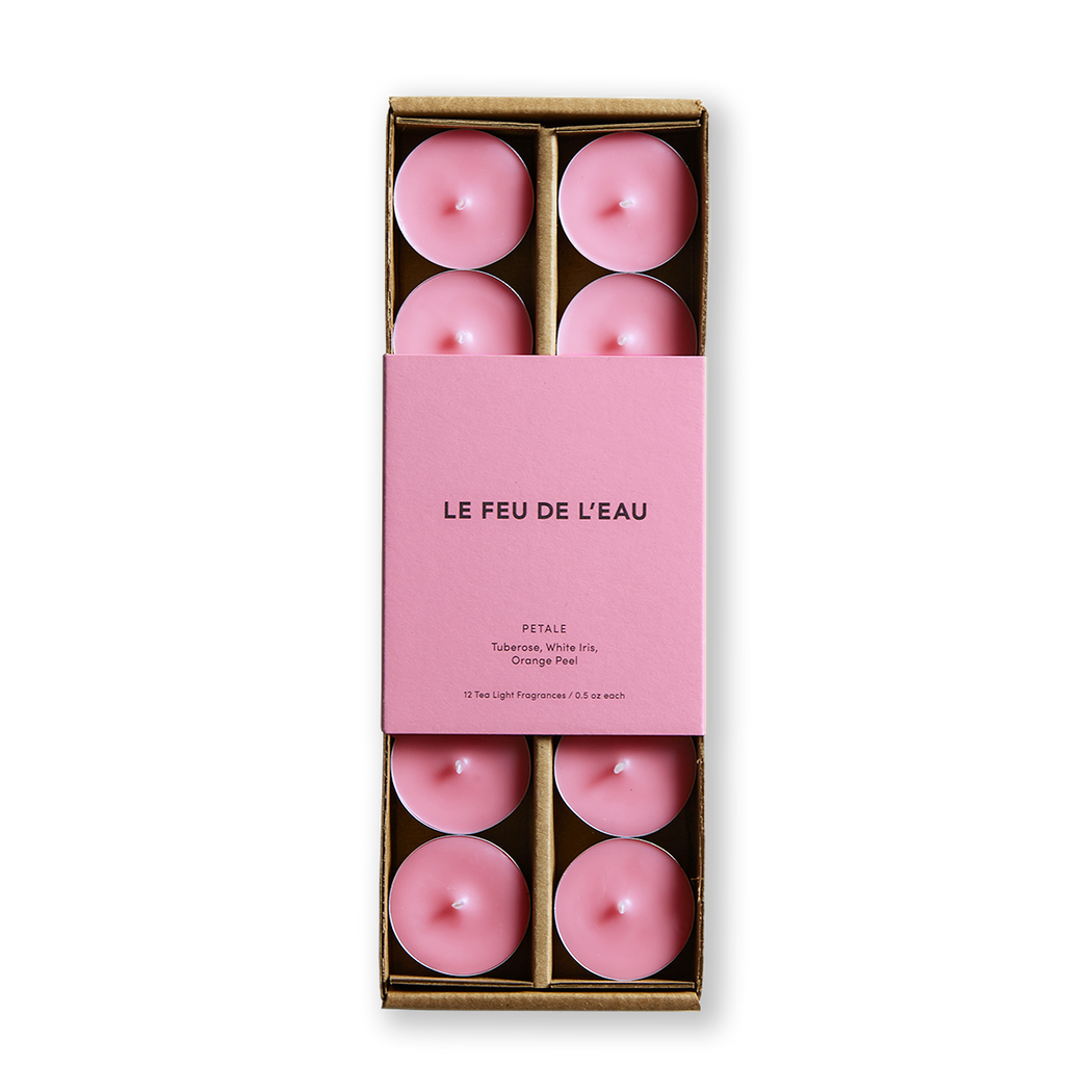 Embrace your full essence with Le Feu De L'eau Petale scented tea light candles. Let tuberose, white iris, and orange peel enchant your senses. Set of 12, cruelty-free, coconut apricot wax, and natural fragrance tea lights. Clean burn, lead-free wicks. Made in Los Angeles. Image is of set of 12 pink scented tea lights in box with matching pink packaging.