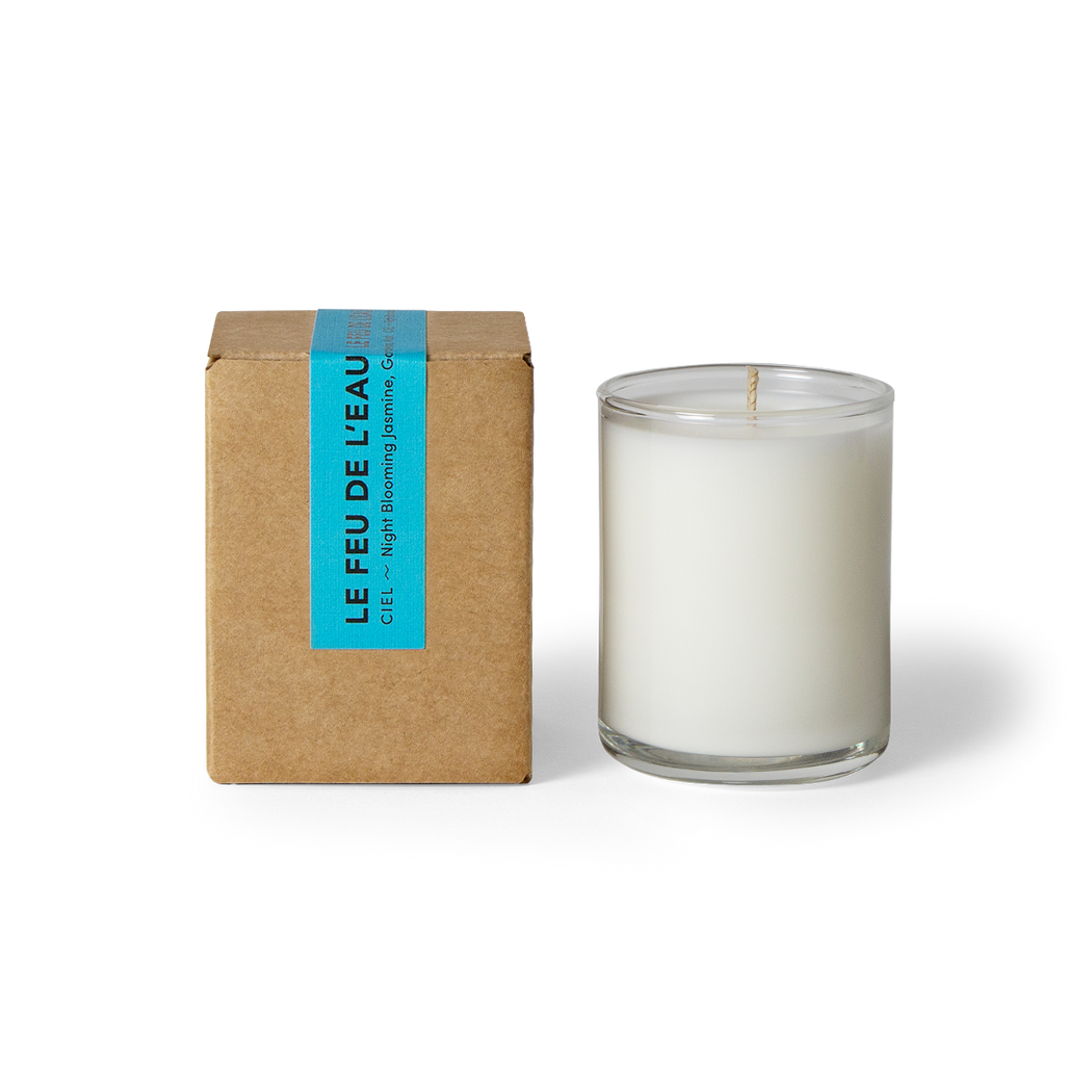 Indulge in the 3oz Ciel glass candle, blending night blooming jasmine, gardenia and musk. Hand-poured in LA, cruelty-free, with coconut apricot wax, natural fragrance, and lead-free cotton wicks. No harmful additives. The candle is displayed unboxed, positioned beside its packaging, set against a clean white backdrop.