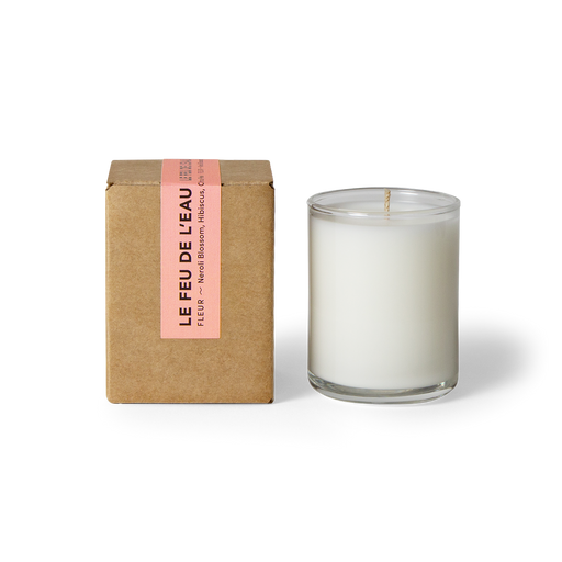 Discover the 3oz Fleur glass candle, blending neroli blossom, hibiscus, and citrus peel. Spring awakens with the liveliness of citrus cradled inside the warmth of neroli and ylang ylang. Hand-poured in LA, cruelty-free, with coconut apricot wax, natural fragrance, and lead-free cotton wicks. No harmful additives. The candle is displayed unboxed, positioned beside its packaging, set against a clean white backdrop.